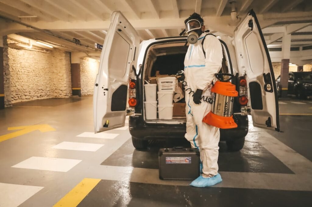 un technicien de désinsectisation qui porte un pulvérisateur et un masque